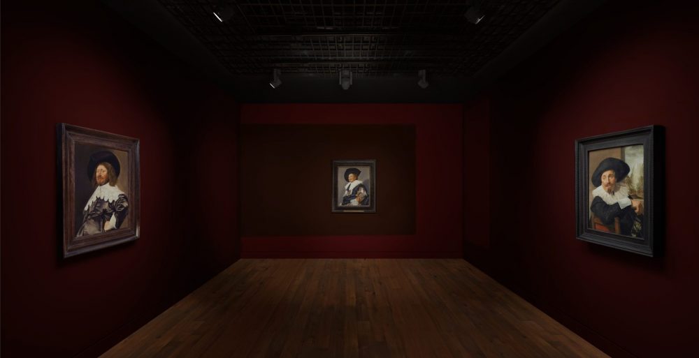 A dark red gallery with wooden floors in which 3 paintings by Frans Hals are hung, including The Laughing Cavalier